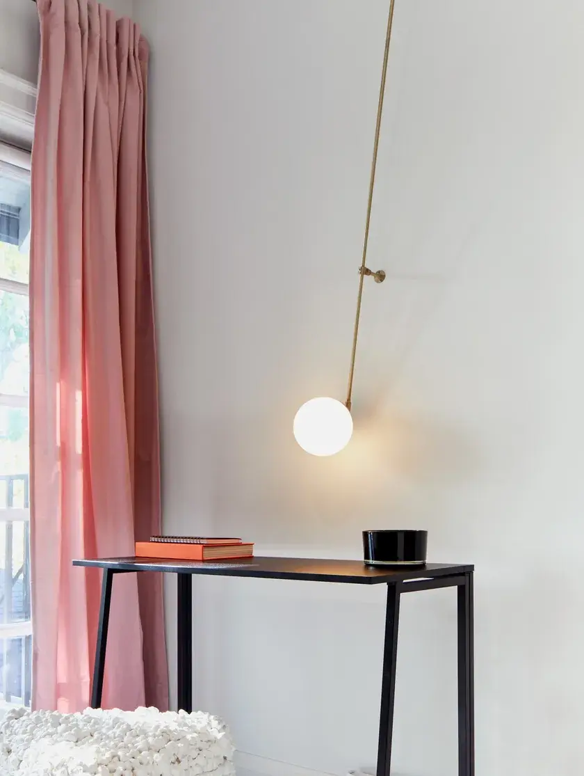 a black desk by a window with pink curtains and a tall gold globe sconce
