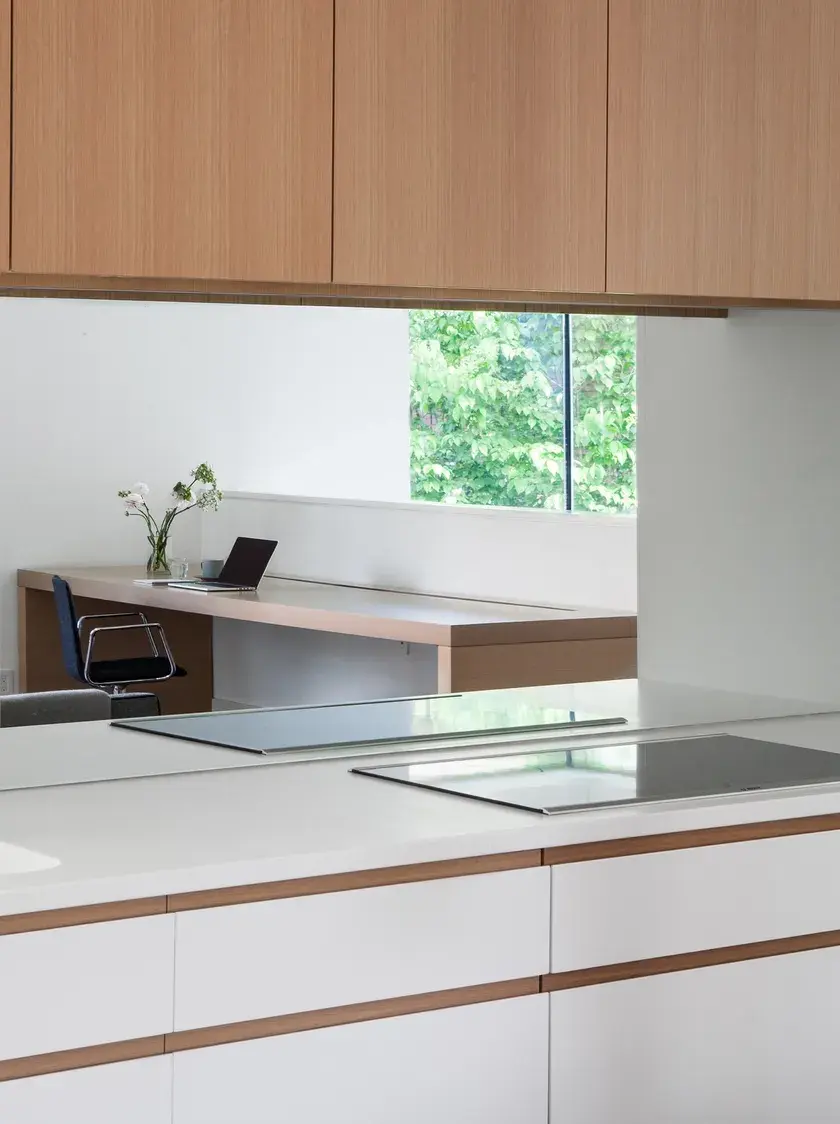 a kitchen counter with a mirrored backsplash and an office setup in its reflection