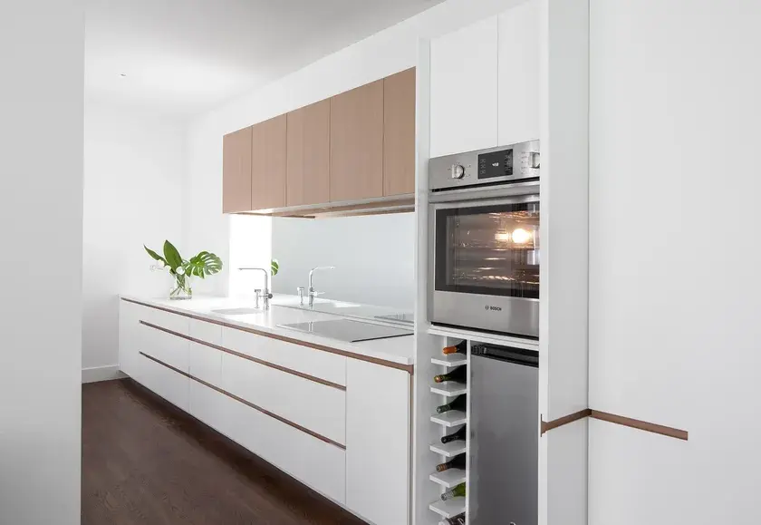 a white single line kitchen with caesarstone countertops, a mirrored backsplash, and an oven and wine cellier tucked behind cabinet doors