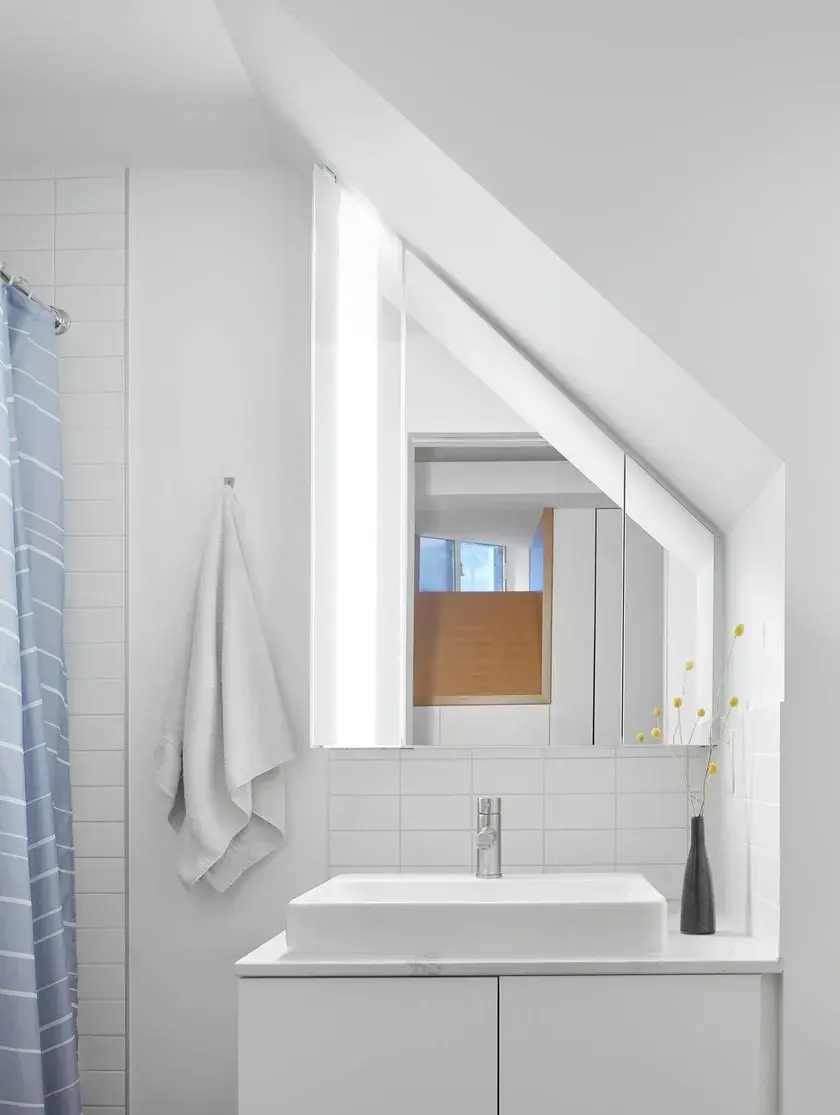 an all white bathroom facing the vanity with a small vessel sink and an asymmetrical ceiling volume