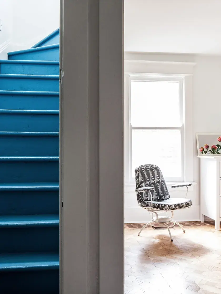 a royal blue winding staircase to the left, and the entry to a white bedroom with a white dresser and striped chair