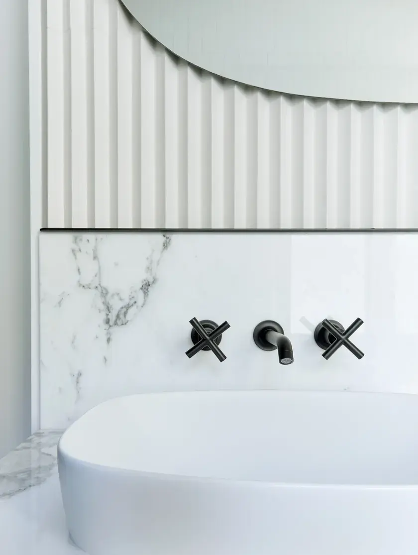 close up of a bathroom with a white vessel sink in, on top of a light grey quartz, and off-white bevelled backsplash and black fixtures