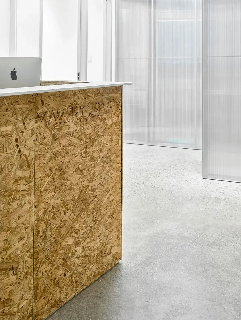 a close up of a reception desk made of plywood, above untreated concrete floors, against polycarbonate panels