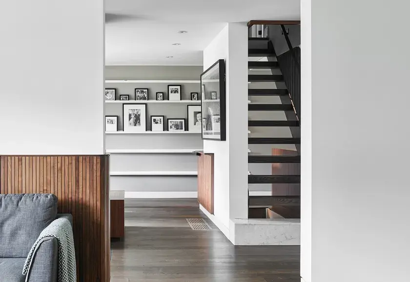 a hallway facing the entrance to a room with smoked oak floors and walnut millwork panelling on the wall, and a black staircase with floating steps