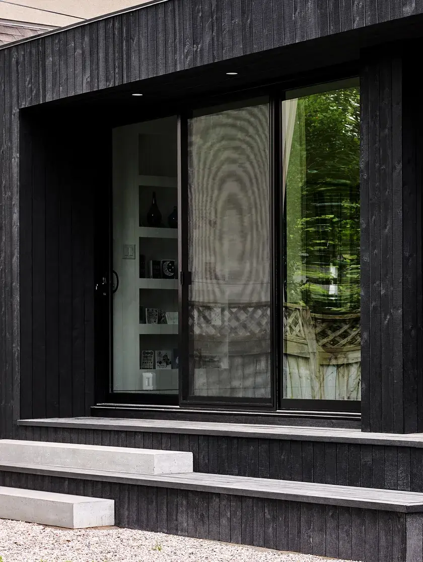 a close up of a blackened wood-clad volume addition and large sliding doors