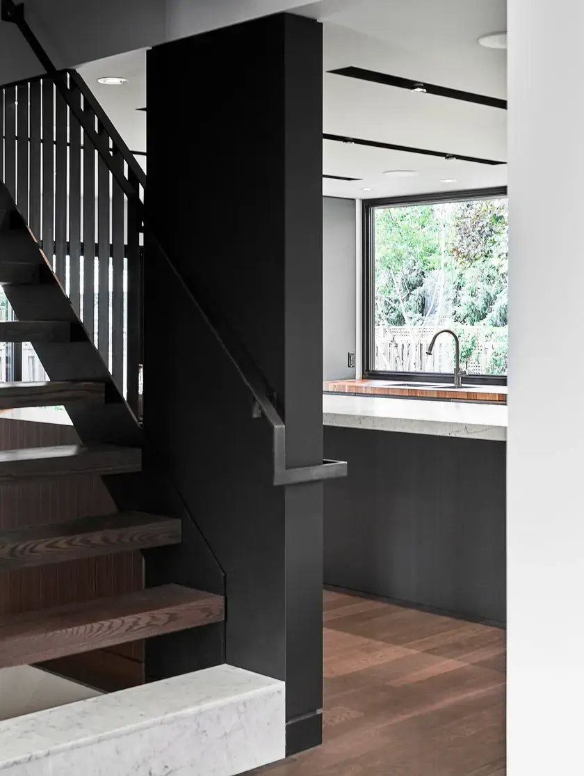 a close up of a staircase with dark smoked oak steps, a black accent wall, and a kitchen in the background