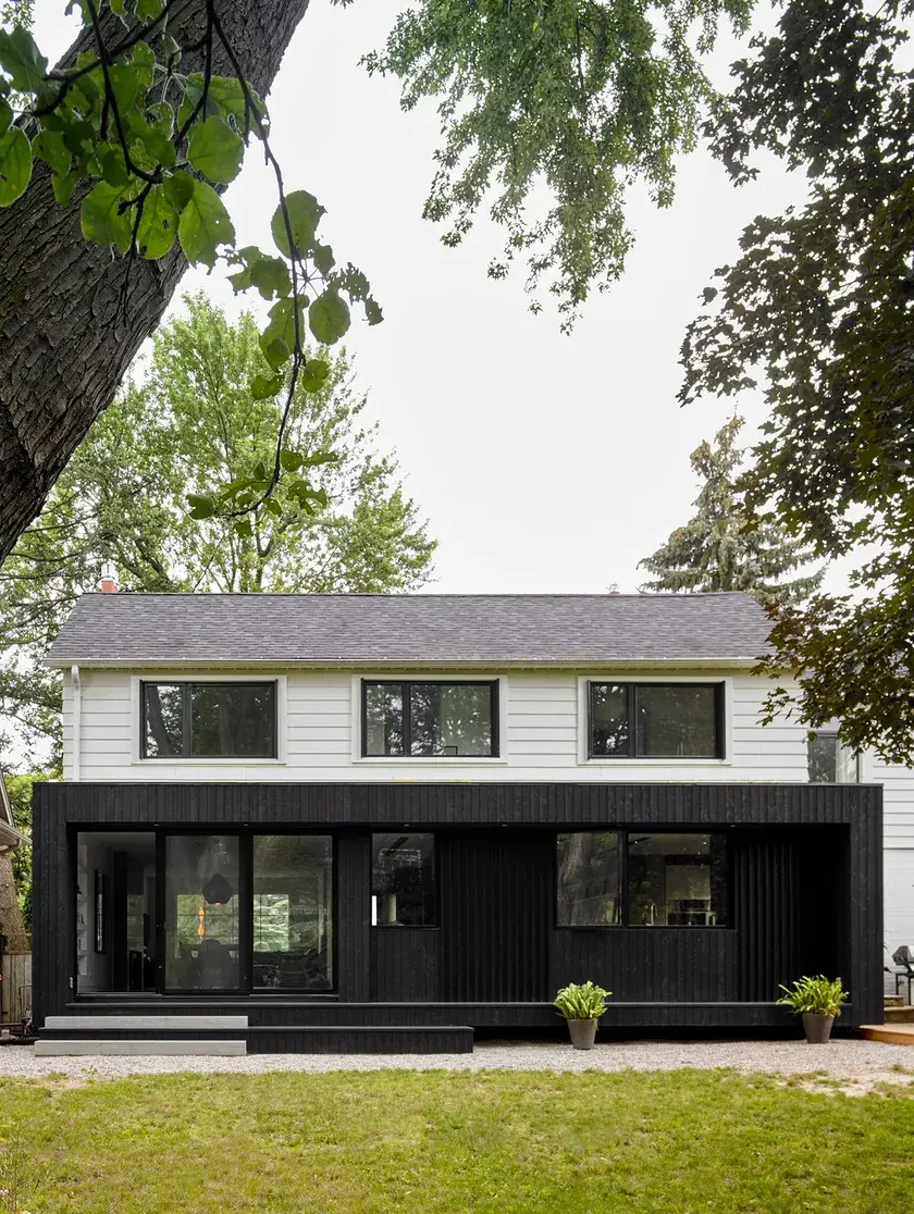 the backyard of a home with a blackened wood-clad volume addition and large sliding doors on the first floor, white panelling on the second floor