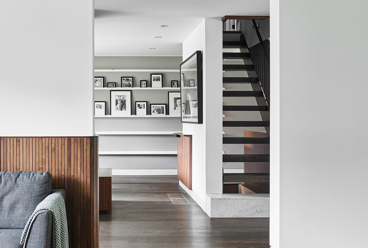 a hallway facing the entrance to a room with smoked oak floors and walnut millwork panelling on the wall, and a black staircase with floating steps