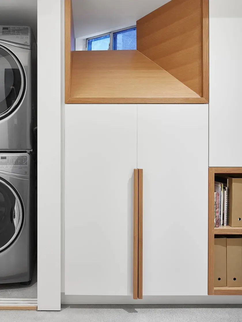 A laundry facility tucked behind a whit continuous millwork wall with solid oak handles