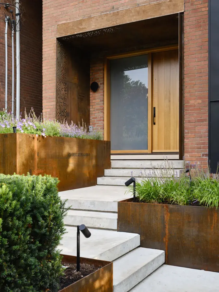 A front walkway to the entrance of a home with red brick, blackened metal and weathered steel