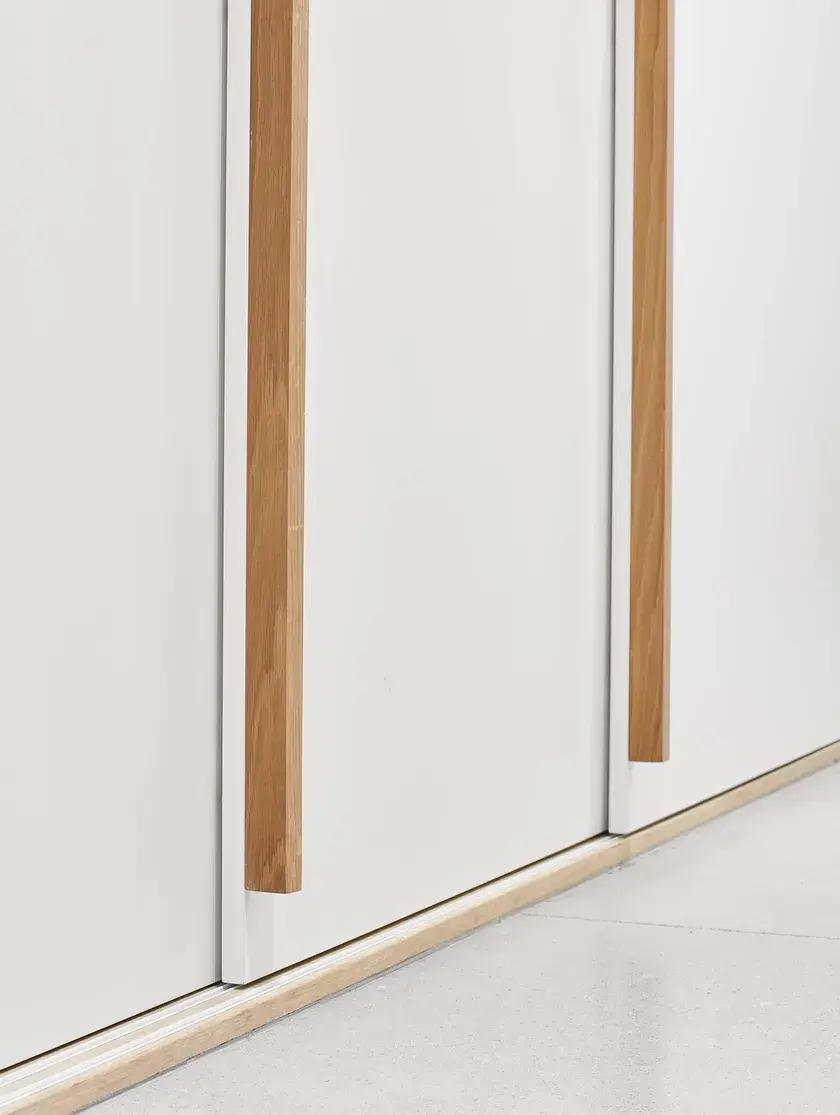 close up of a continuous white millwork wall with solid oak handles, and polished concrete flooring