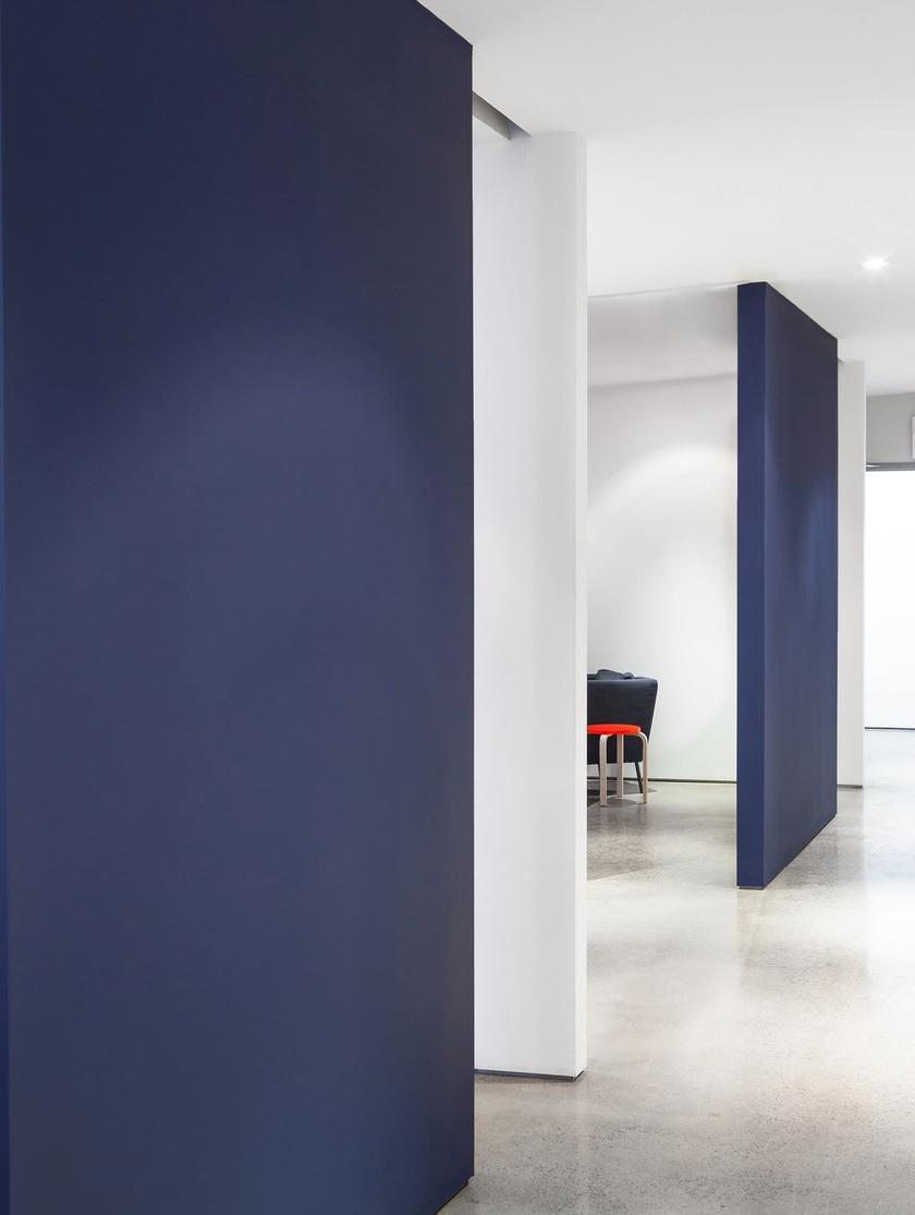 a hallway with two office rooms concrete floors, white walls, and navy blue, floor to ceiling sliding doors
