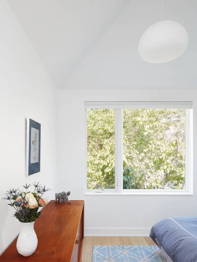all white bedroom with a window facing trees