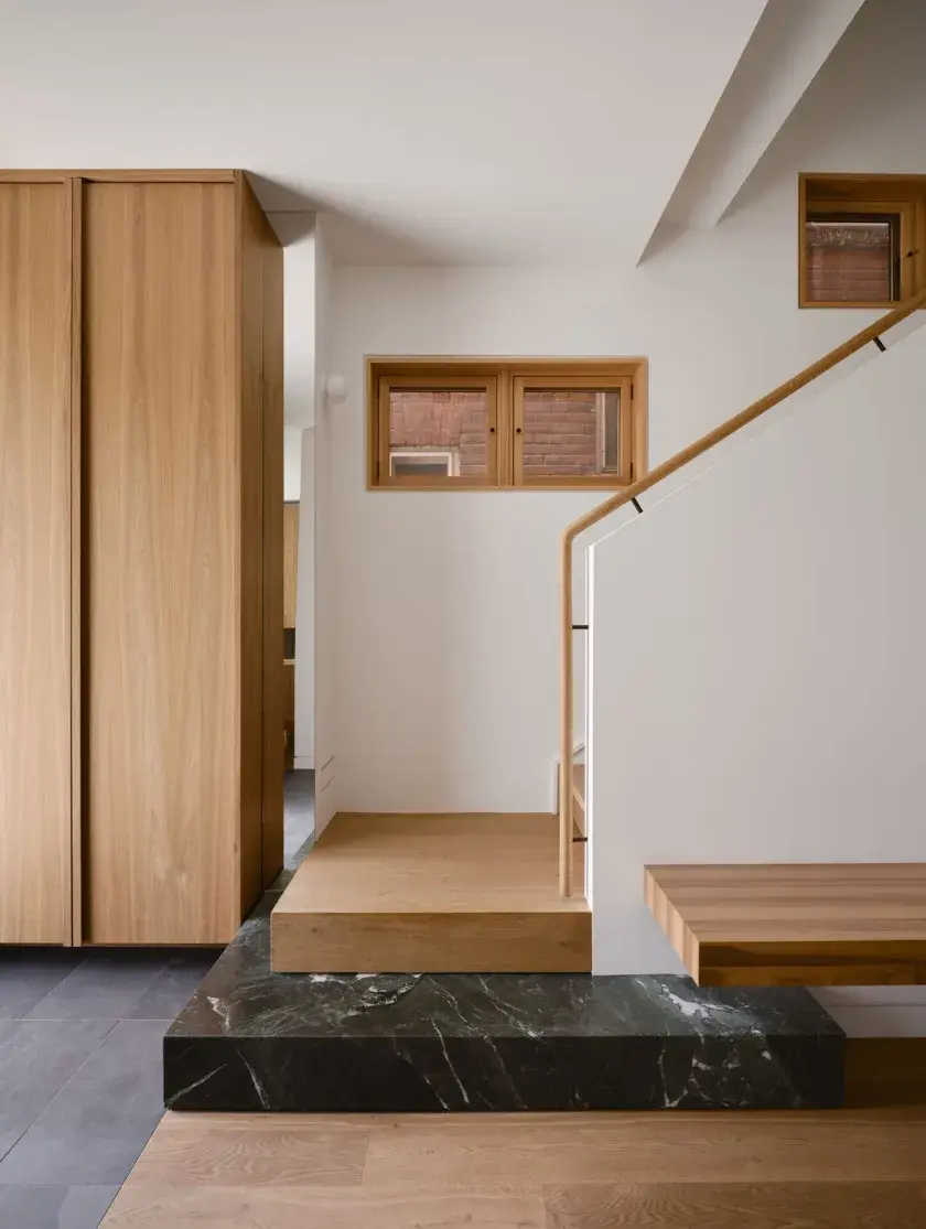 Interior entrance to a home directly facing an ascending stairway. Materials include white oak flooring and handrail, slate tile, honed marble, and walnut millwork