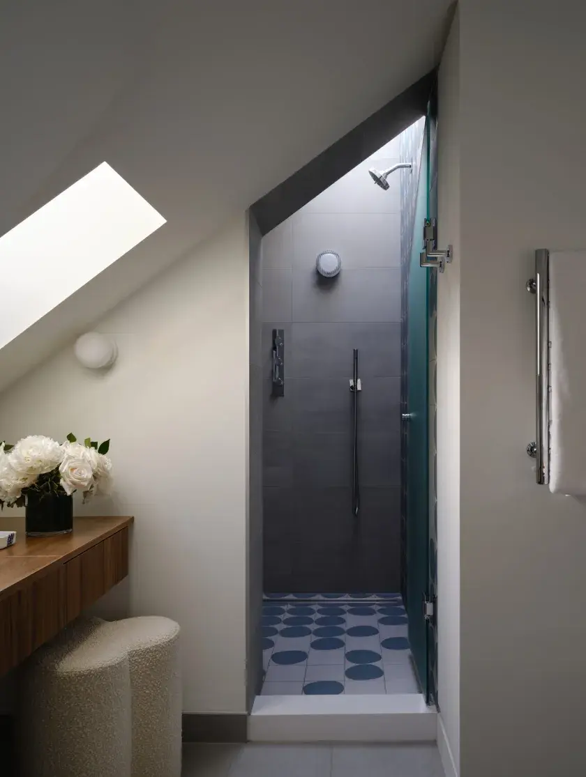 An ensuite shower with grey slate tiles, light blue spot patterned floor tiles, a skylight, and a custom millwork vanity in the foreground to the left